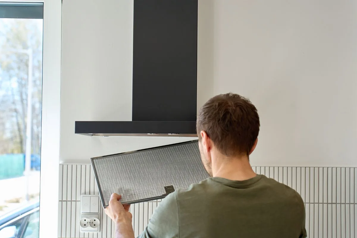 technician removing a clogged grease filter from a range hood vent